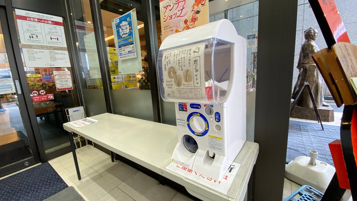 東京・銀座のアンテナショップ「まるごと高知」の入口前に置かれた鹿の角ガチャ。ガラス扉の横、台の上に白いガチャがある。